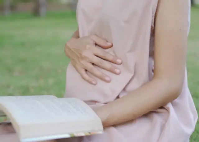 pregnant girl holding hand on belly and reading book